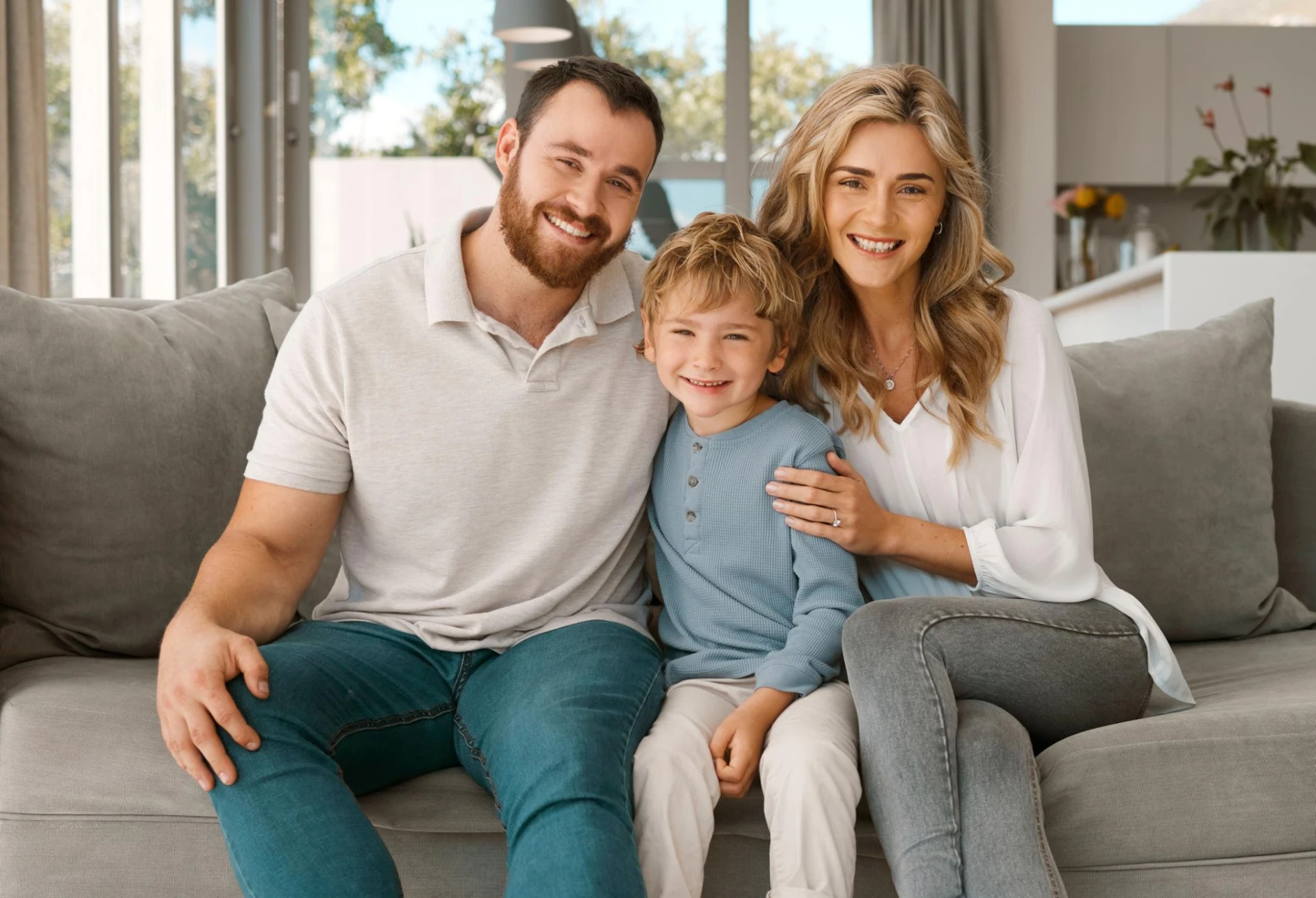 A smiling couple and their young son sitting together on a living room couch